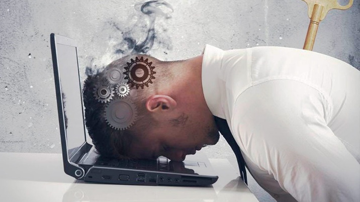 Un hombre, cuyo cerebro son ruedas de un engranaje, apoya su cabeza agotado sobre el teclado de su ordenador portátil